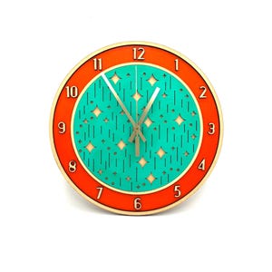 May include: A turquoise and orange wall clock with a geometric pattern and silver hands. The numbers 1 through 12 are displayed on the outer edge of the clock.
