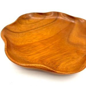 May include: A wooden serving tray with a wavy edge. The tray is made of light brown wood and has a natural finish.