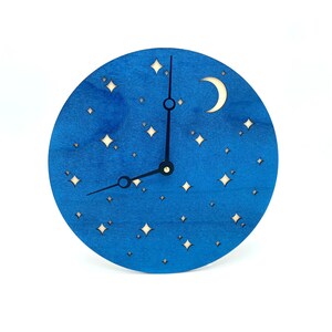 May include: A blue wooden clock with a crescent moon and stars cut out. The clock hands are black.