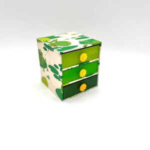 May include: A small green and white drawer organizer with three drawers. Each drawer has a yellow flower-shaped knob.