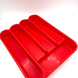 May include: A bright red plastic cutlery tray featuring four long, narrow vertical compartments and one wider horizontal compartment at the top. The organizer has a smooth, glossy finish and rounded corners, designed for kitchen drawer storage.