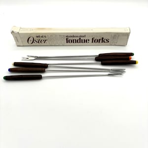 May include: A set of six stainless steel fondue forks with brown wooden handles. The forks are packaged in a white box with the text "Oster fondue forks" printed on it.
