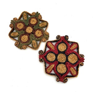 May include: Two woven trivets with a geometric design. One trivet is green, brown, and tan. The other trivet is red, black, and tan.