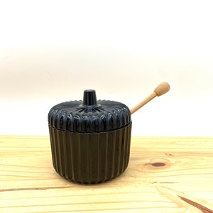 May include: Black ceramic honey pot with a ribbed design and a wooden honey dipper.