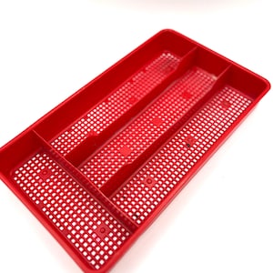 May include: A rectangular red plastic drawer organizer tray featuring a grid-patterned base with small square perforations. The tray is divided into three distinct longitudinal compartments by two integrated vertical dividers for storage.