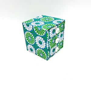 May include: A small, square, four-drawer storage box with a green and white floral pattern. The drawers have white knobs.