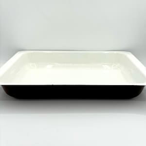 May include: A white enamel baking dish with a black rim. The dish is empty and ready to be used for baking.
