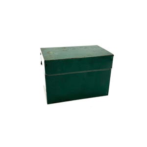 May include: A vintage, dark green metal box with a rectangular shape. The box has a hinged lid and appears to be made of painted steel. The box is likely used for storage and has a slightly distressed appearance.