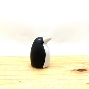 May include: A small, black and white ceramic penguin figurine. The penguin is standing upright on a wooden surface.