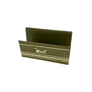 May include: A rectangular olive green mail holder featuring a high back panel and a shorter front panel. The front panel displays the word Mail in white cursive script above a decorative white horizontal border with a repeating scroll pattern.