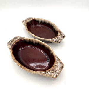May include: Two brown and white glazed ceramic oval baking dishes with handles.
