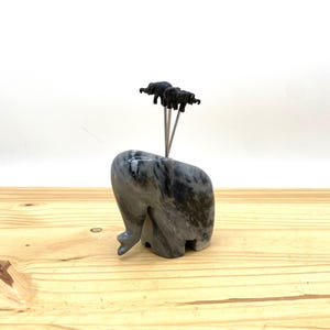 Puede incluir: Una figurita de elefante de mármol gris con cuatro pequeños porta palillos de dientes de elefante negro en la parte superior.