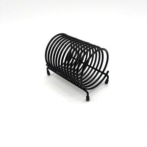 May include: Black metal magazine rack with a spring-like design. The rack is made of wire and has a cylindrical shape.