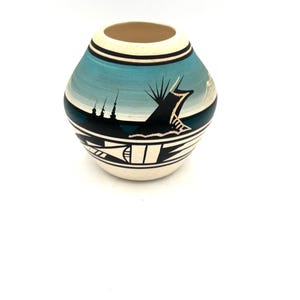 May include: A small, white ceramic pot with a blue and black geometric design. The pot has a rounded shape and a wide opening.