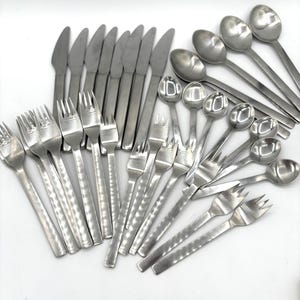 May include: A collection of stainless steel silverware, including knives, forks, and spoons. The silverware has a hammered texture on the handles and a polished finish. The arrangement suggests a complete dining set.