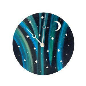 Pode incluir: Um relógio de parede redondo com um design de céu noturno pintado. O mostrador do relógio apresenta tons de azul e verde, com uma lua crescente e recortes em forma de estrela. Os ponteiros prateados indicam as horas.