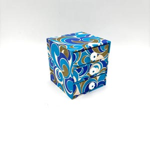 May include: A small, three-drawer dresser with a blue, white, and brown swirl pattern. Each drawer has a white flower-shaped knob.
