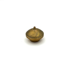 May include: A small, antique-style, gold-colored metal knob with a rounded, textured top and a small, cylindrical stem. The knob has a slightly weathered appearance, suggesting age or a vintage aesthetic. It is set against a plain white background.