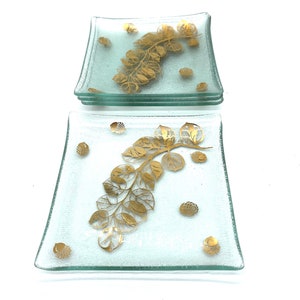 May include: Set of four clear glass square plates with a gold leaf design. The plates have a frosted glass finish and feature a gold leaf branch with leaves and small gold dots.
