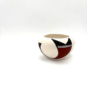 May include: A white ceramic bowl with a geometric design in black and red. The bowl is round and has a slightly flared rim.