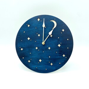 May include: A blue wooden clock with a crescent moon and stars cut out. The clock hands are white and gold.