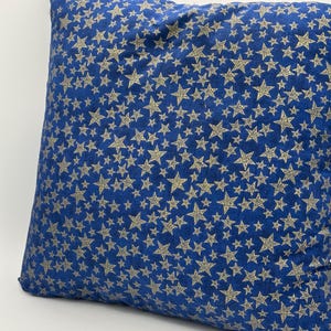 May include: A square throw pillow featuring a deep blue fabric base covered in a dense, repeating pattern of small, metallic gold-colored stars of varying sizes. The stars are distributed across the entire surface of the blue textile cover.