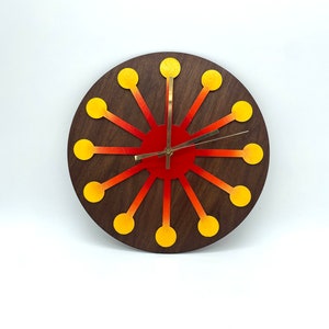 May include: A round wooden clock with a red and orange gradient background. The clock has a gold-colored frame and hands, and yellow circles around the edge.