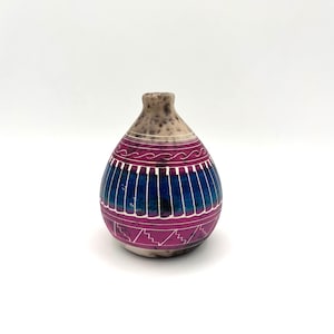 May include: A small, teardrop-shaped ceramic vase with a white background and a pink and blue geometric design.