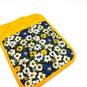 May include: A yellow quilted oven mitt with a floral pattern. The mitt features a square design with a yellow border and a fabric panel covered in white, blue, and yellow flowers on a dark background.