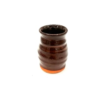 May include: A small, brown ceramic mug with a textured, wavy design and an orange rim.