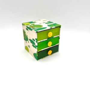 May include: A small green and white drawer organiser with three drawers. Each drawer has a yellow flower-shaped knob.