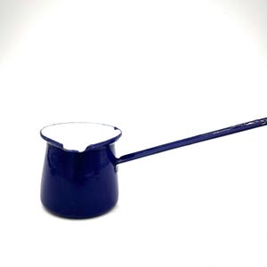 May include: A small, navy blue enamel coffee pot with a long handle. The interior of the pot is white. The pot is designed for stovetop use. The handle is attached to the side of the pot and extends outward.