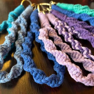 Könnte beinhalten: Ein Set aus sechs bunten gehäkelten Schlüsselanhängern in Blautönen, Lila und Grün. Die Schlüsselanhänger sind aus dickem, strukturiertem Garn gefertigt und haben ein schlichtes, elegantes Design.