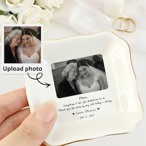 May include: A white ceramic trinket dish with a gold rim, featuring a black and white photo and handwritten text. The dish has a square shape with wavy edges. The text reads "Mom, Everything I am you helped me to be. Thank you for being by my side today & always. Love, Olivia Feb 12, 2023."