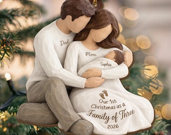 May include: A hanging ornament featuring a sculpted family of three with a parent figure labeled Dad, a parent figure labeled Mom, and a baby labeled Sophia. The text reads Our 1st Christmas as a Family of Three 2026 with two small footprints.
