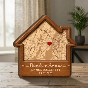 May include: A wooden house-shaped map with a heart marking a location. The map is light brown, framed by a darker wood. The names "David & Emma", address, and date are inscribed on the bottom.