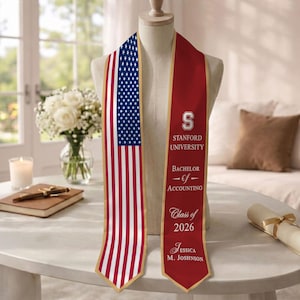 May include: A graduation stole with an American flag design on one side and maroon fabric on the other. The maroon side features the Stanford University logo, "Bachelor of Accounting," "Class of 2026," and a graduate's name.