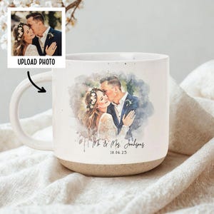May include: White ceramic mug with a watercolor-style image of a couple kissing. The mug has a speckled finish and a tan base. Text on the mug reads "Mr. & Mrs. Johnson" and "18.06.25". A small photo with the text "UPLOAD PHOTO" is also visible.
