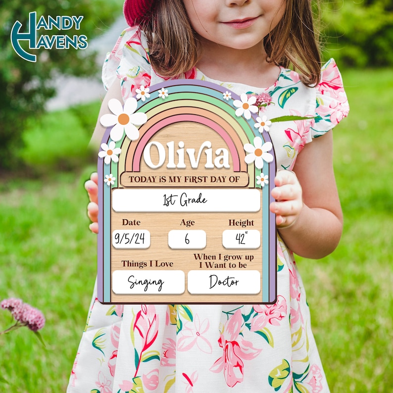 May include: A wooden sign with a rainbow and daisies, personalized with the name "Olivia". The sign says "Today is my first day of 1st Grade". It also includes the date "9/5/24", age "6", height "42", things I love "Singing", and when I grow up I want to be "Doctor".