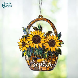 May include: A stained glass sunflower basket with the name "Sophia". The brown basket has a woven handle and holds three yellow sunflowers with brown centres and green leaves. It hangs from a silver chain.
