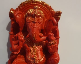 May include: Red Ganesha statue with gold accents. The statue is sitting on a base with intricate details. The statue is made of a smooth, polished material.