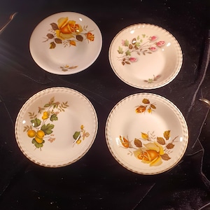 May include: Set of four white ceramic bowls with gold trim. Each bowl features a different floral design with yellow and pink roses, green leaves, and brown stems.