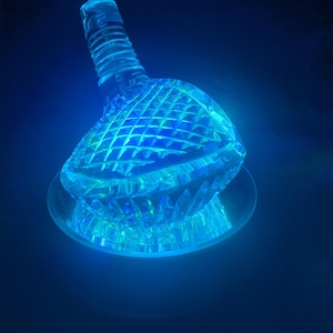 May include: A clear glass bottle with a textured surface and a blue glow. The bottle is sitting on a clear glass base.