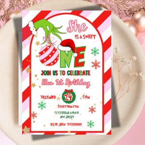 May include: A festive invitation for Elsa's 1st birthday, featuring a Grinch-themed design with a red and white striped border. The invitation includes the text "She is a sweet one" and event details. The invitation is on a white plate.