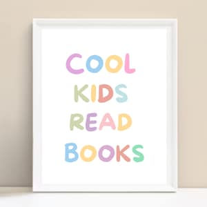 Könnte beinhalten: Ein gerahmter Druck mit dem Text "COOL KIDS READ BOOKS" in Pastellfarben. Der Text ist in einem verspielten, handgeschriebenen Stil gehalten, vor einem weißen Hintergrund. Der Rahmen ist weiß, der Hintergrund hellbeige.