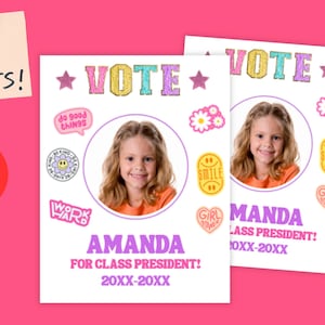 May include: Two white campaign posters with a photo of a smiling girl, the word "VOTE" in colorful letters, and the name "AMANDA" in purple. The posters are on a pink background with a sticky note that says "YOUR VOTE COUNTS!"