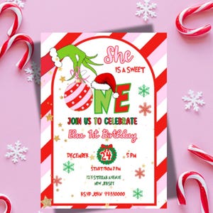 May include: A festive invitation for Elsa's 1st birthday, featuring a Grinch-themed design with a red and white striped ornament and Santa hat. The invitation includes the text "She is a sweet ONE" and event details.