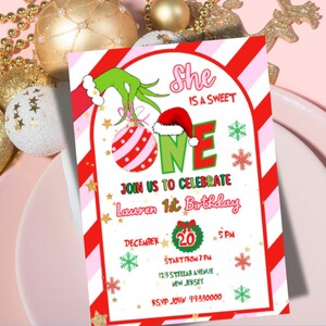 May include: A festive invitation for a first birthday celebration. The design features a Grinch-themed illustration with a red and white striped border. The text reads "She is a sweet ONE" and includes details for the party, such as the date, time, and location.