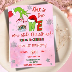 May include: Pink invitation card with the text "She's the ONE who stole Christmas!" and "Elsa 1st Birthday". The card features Grinch-themed graphics and a Santa hat. The date is December 24th.