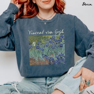 May include: A navy blue sweatshirt with a vintage-style print of a painting by Vincent van Gogh. The painting depicts a field of blue irises.